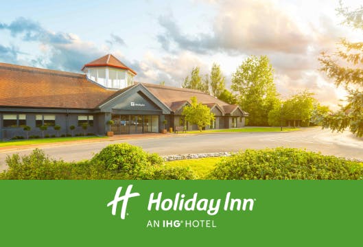 Exterior view of a Holiday Inn with sunlit clouds above and lush greenery surrounding the entrance.