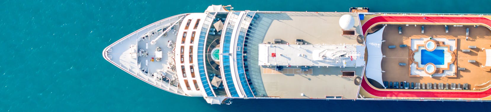 An aerial view of a cruise ship with a large pool deck visible at the rear, and a spacious area with lounge chairs and sunbeds.
