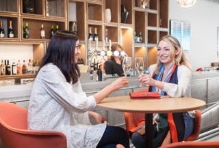 Manchester Airport Lounges - the image shows two happy customers enjoying a glass of wine in one of the Manchester Airport Lounges prior to their flight departing.