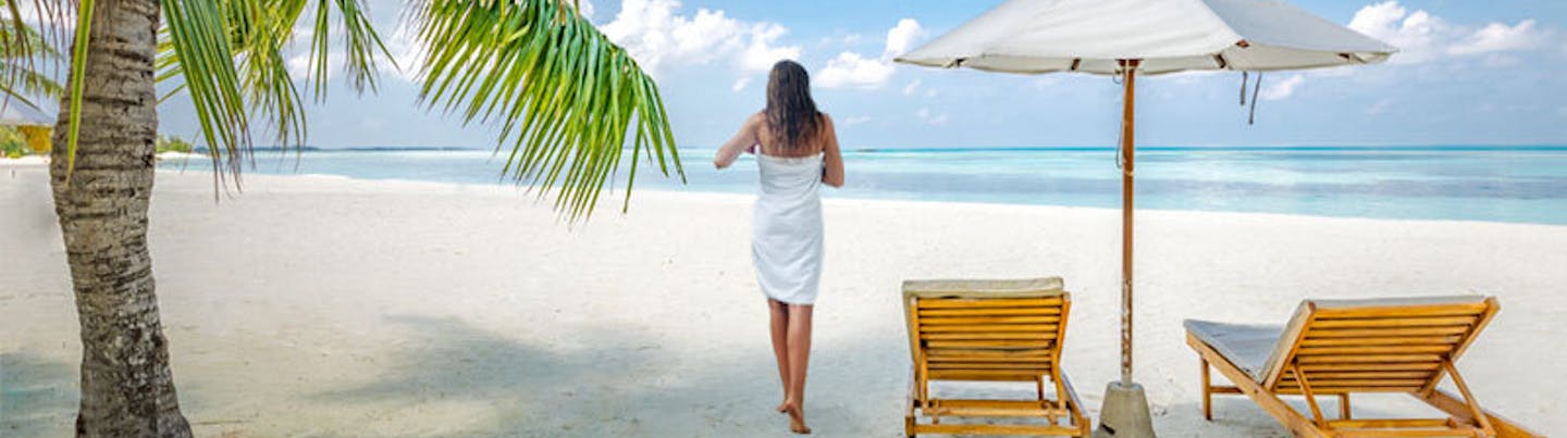 Lady wrapped in beach towel strolling along the beach from her sun lounger to the sea | Change Hassle Free