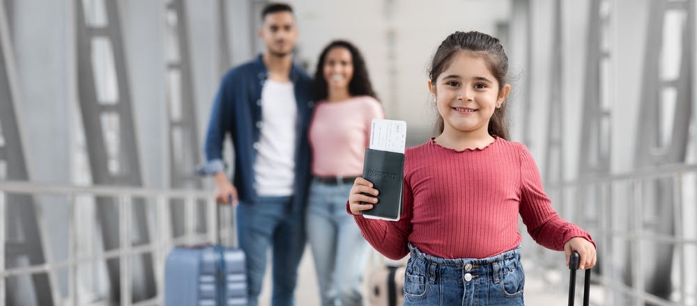 Child holding passport with parents in the background