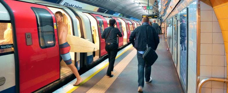 Man wearing shorts and surfboard boarding an underground train.