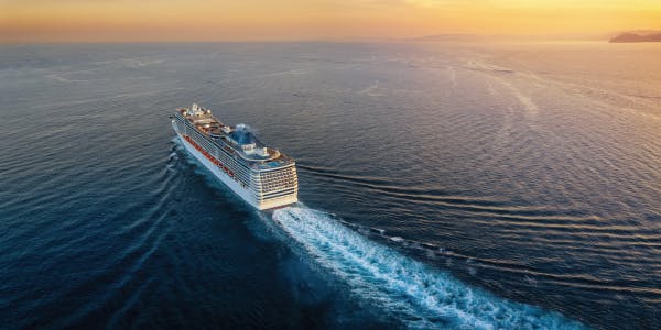 An aerial view of a cruise ship cutting through calm sea waters at sunset, illustrating vaccinations for cruise holidays.