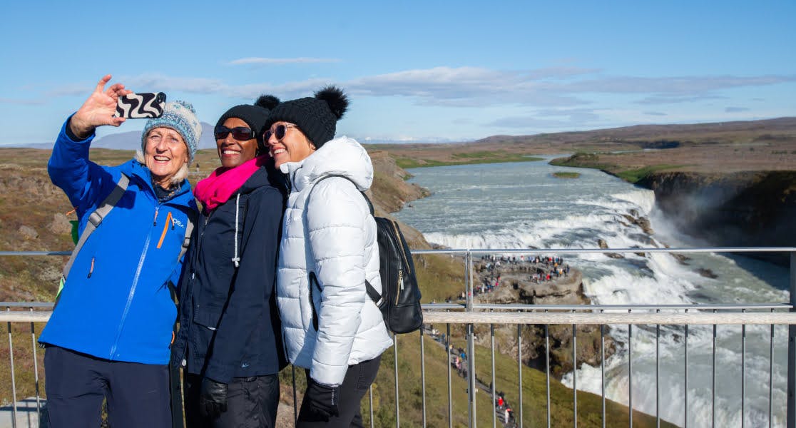 Group of friends taking a selfie at a scenic waterfall stop during a Fred Olsen cruise excursion, with Fred Olsen cruise insurance ensuring hassle-free travel