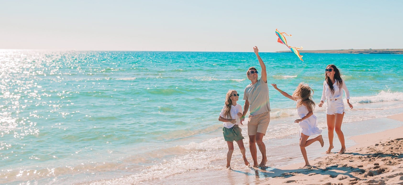 family of 4 playing on the beach and flying a kite together