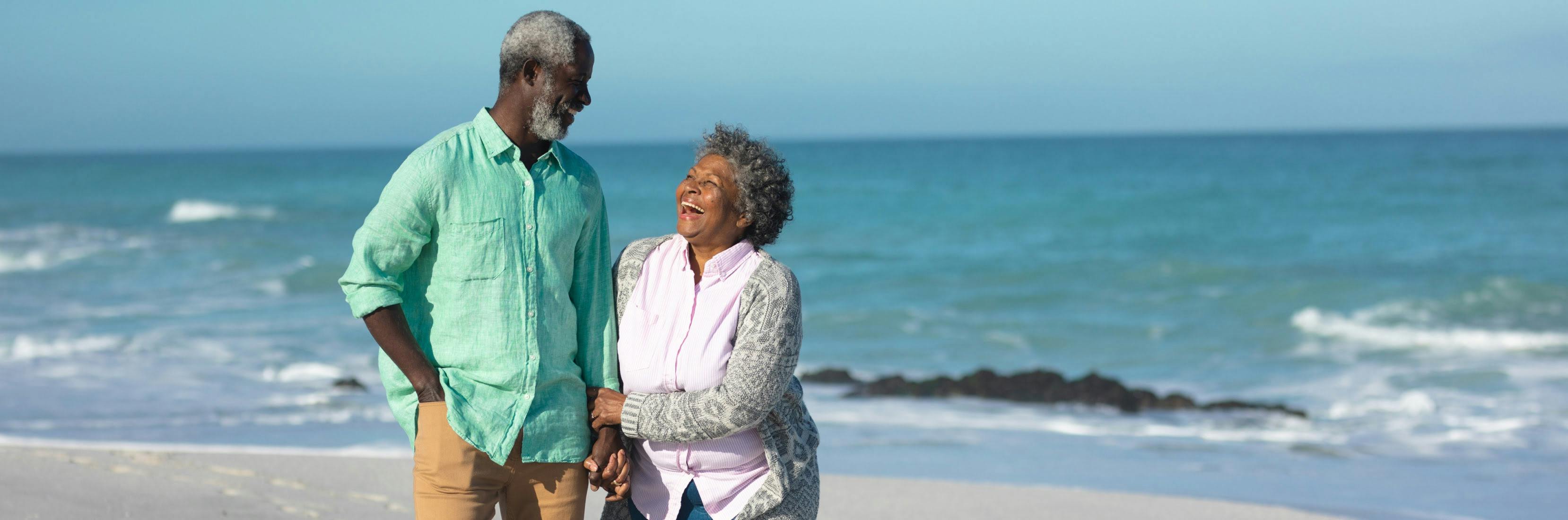An older couple stroll hand-in-hand along a sunlit beach, their joyful laughter reflecting the peace of mind provided by travel insurance for over 70's.
