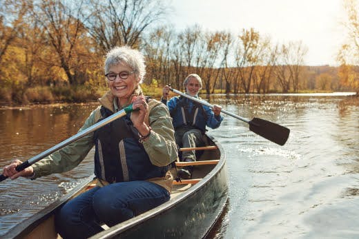 Two older adults paddling a canoe on a calm river during autumn, showing relaxing outdoor adventures for all ages.