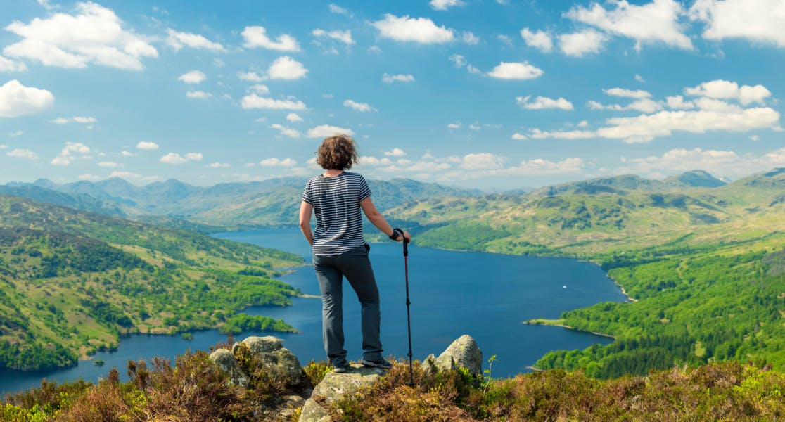 Backpacker standing on a rocky hilltop overlooking a vast lake and rolling hills, exploring with confidence thanks to backpacker travel insurance
