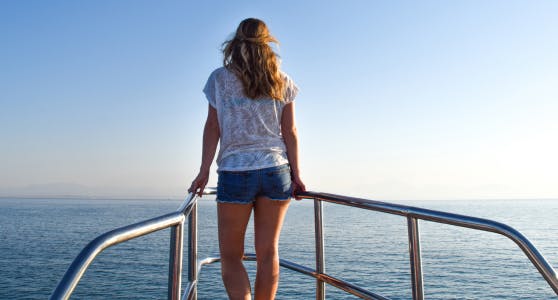 Woman standing at the bow of a boat, looking out to sea on a peaceful holiday, confidently covered by insurance for medical conditions