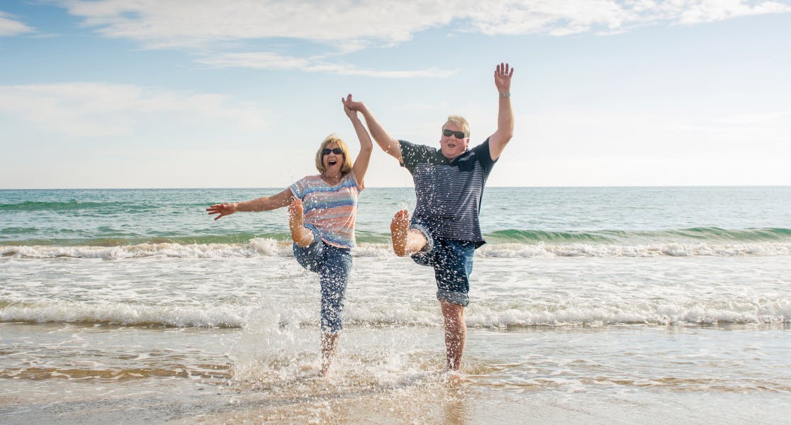 Happy older couple splashing in the sea on a sunny beach holiday, enjoying peace of mind with single travel insurance