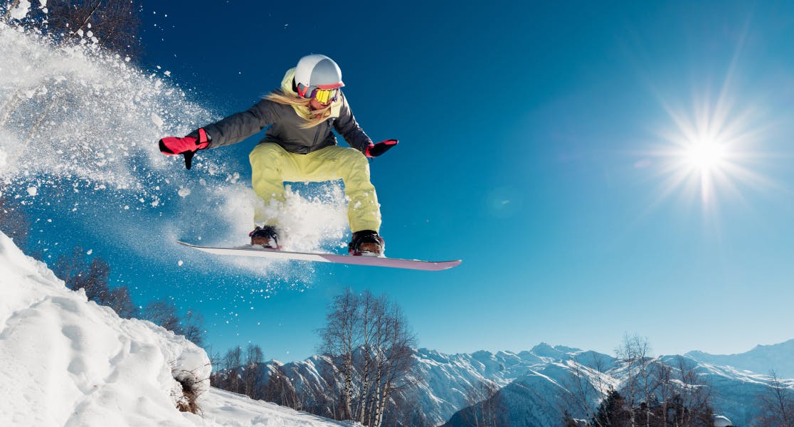 Snowboarder catching air on a bright, sunny day in the mountains, fully protected with winter sports insurance
