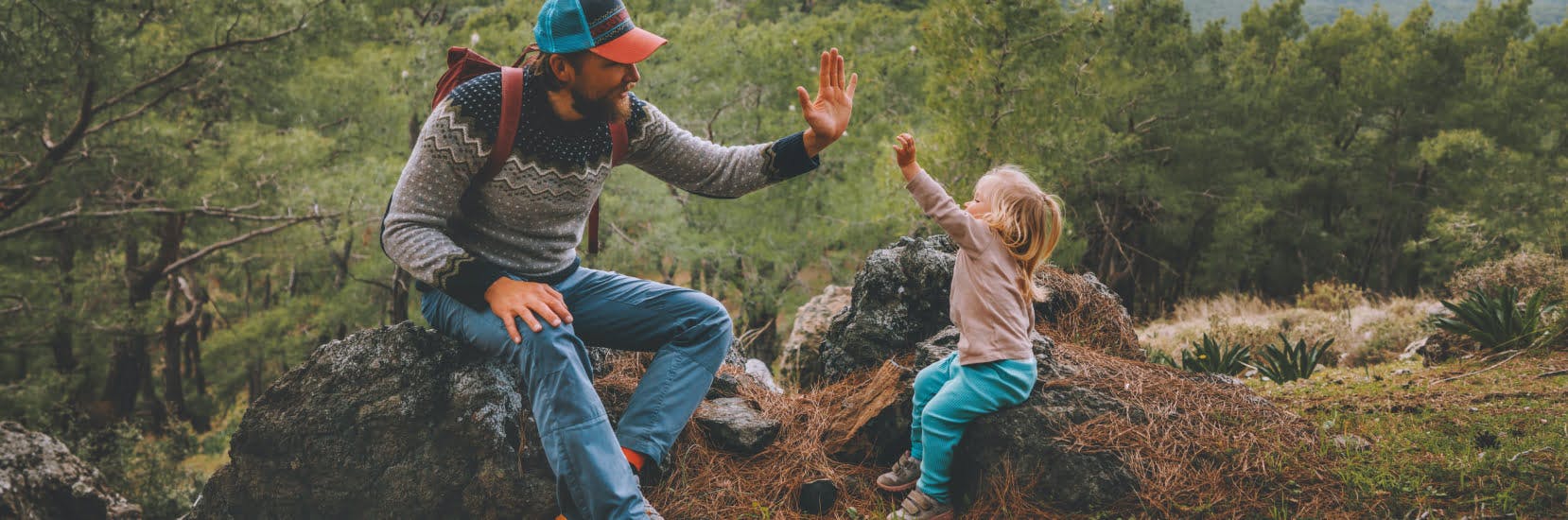 A single parent and child enjoying a hike in nature, sitting on rocks and sharing a high five — perfect for illustrating single parent travel insurance.