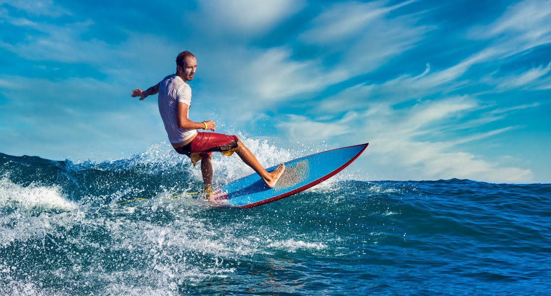 A man surfing across a wave on a sunny day, symbolising adventure holidays and active travel experiences.