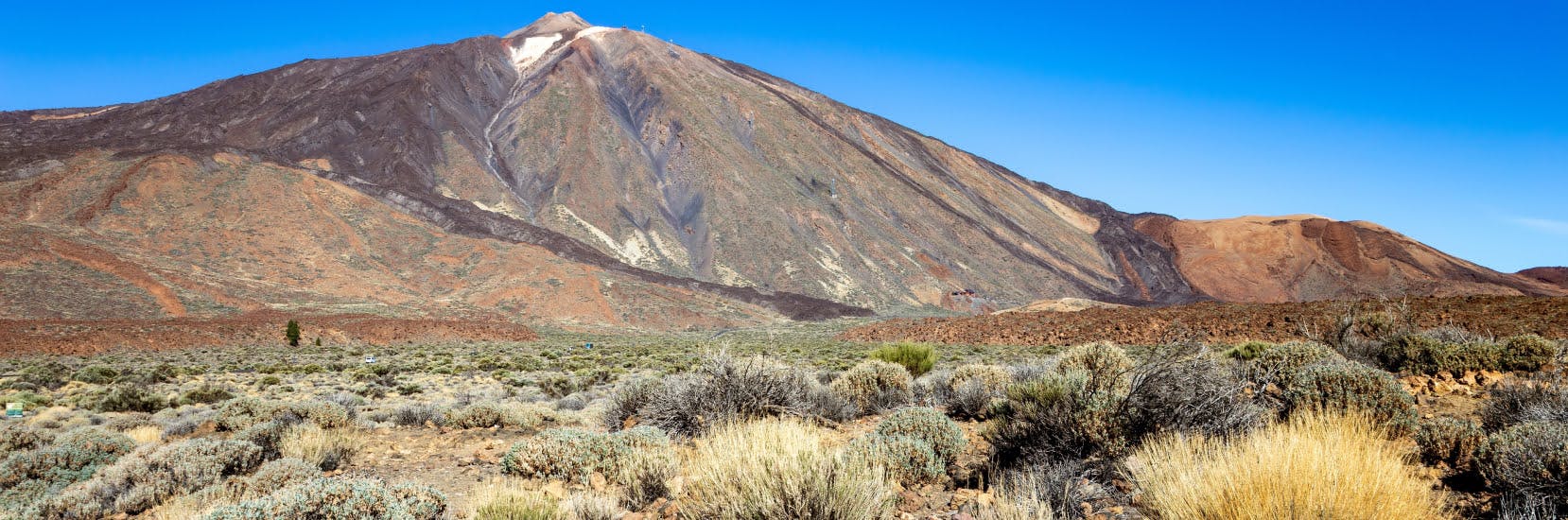 Panoramic view of Mount Teide, Tenerife's famous volcanic peak surrounded by rugged terrain under a clear blue sky, ideal for adventure travellers considering travel insurance for Tenerife trips.