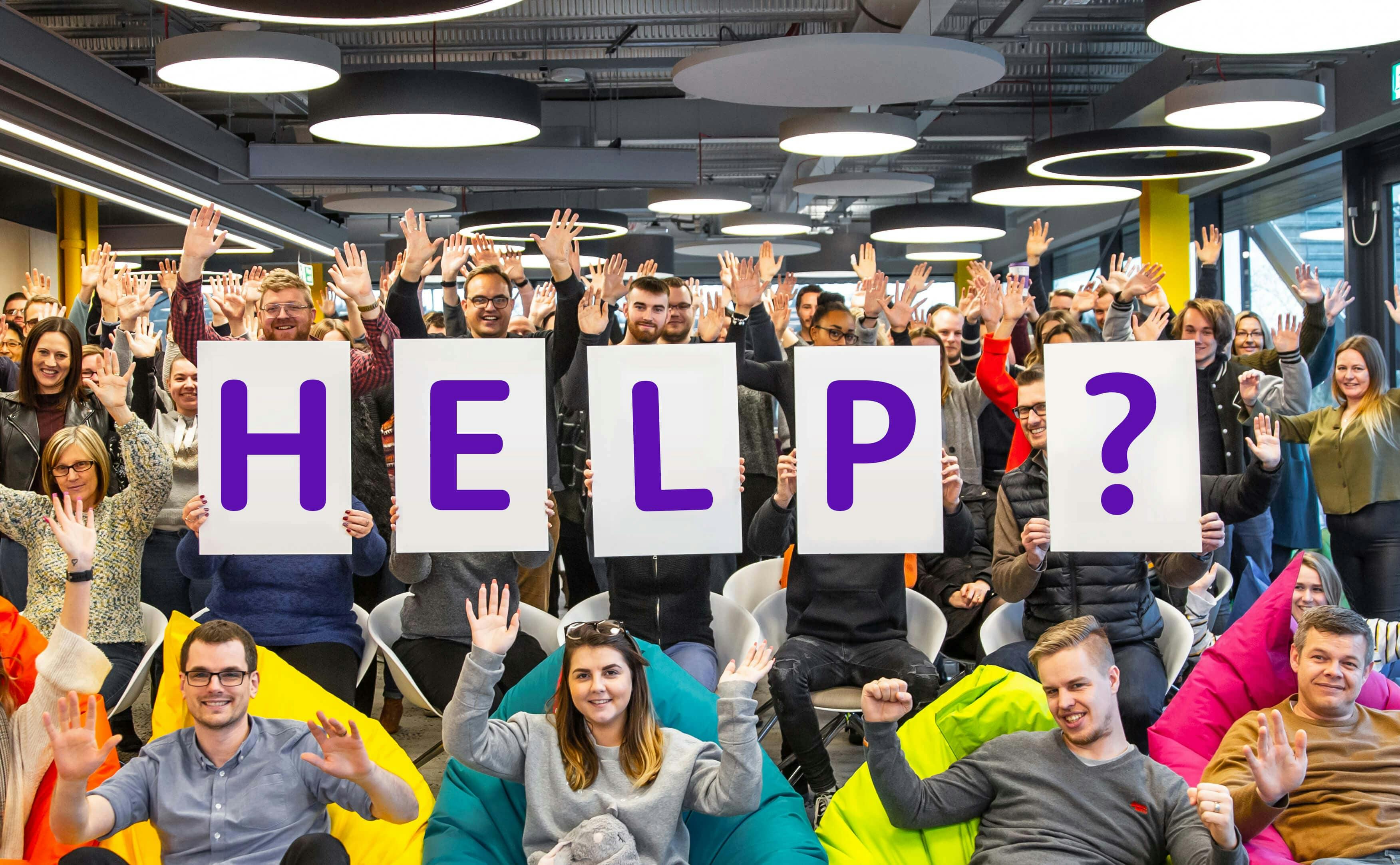 The holiday Extras team raising their hands, with four individuals in the front holding signs that spell out 'HELP?' in bold purple letters.
