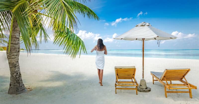 A woman in a white towel walks towards the turquoise ocean on a pristine tropical beach