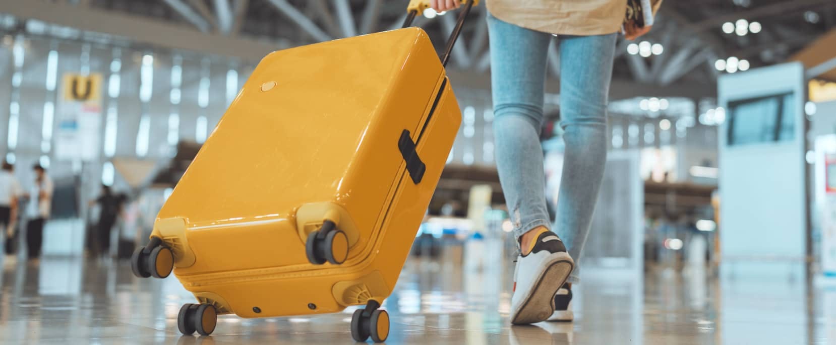 A traveler pulling a bright yellow suitcase through a modern airport terminal.
