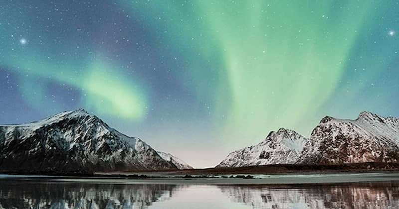The Northern Lights cast a green glow over a snow-covered mountain landscape