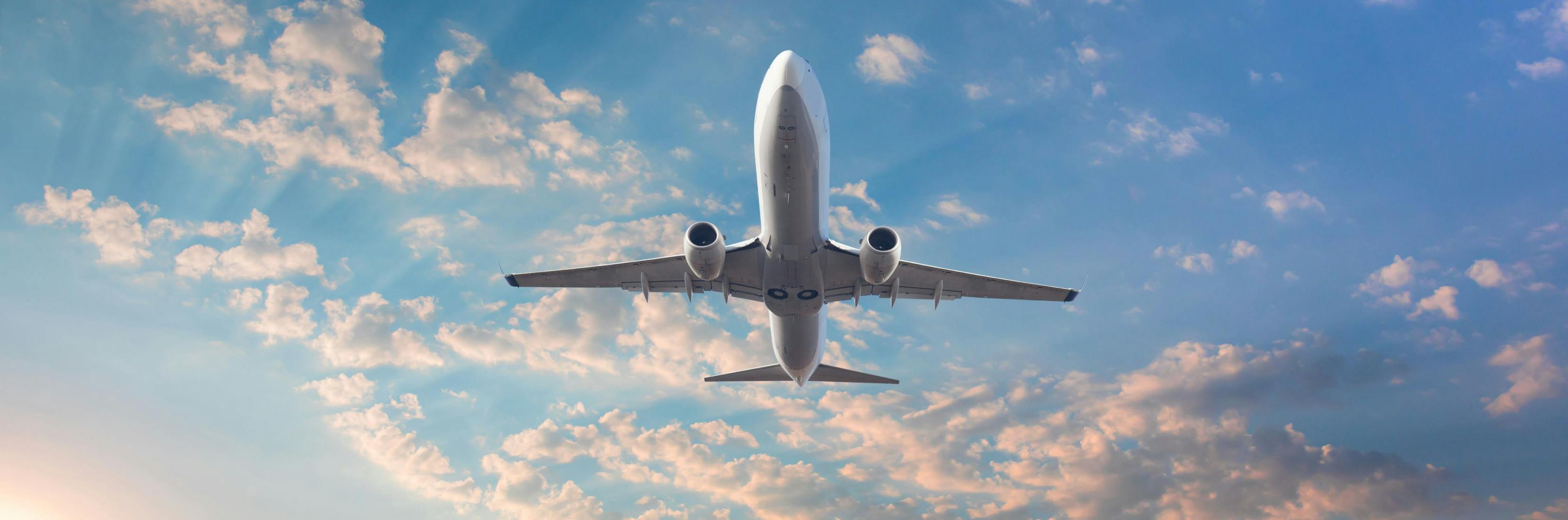 A commercial airplane flying through a bright, partly cloudy sky, symbolising the freedom and extended trips often associated with long-stay travel insurance.