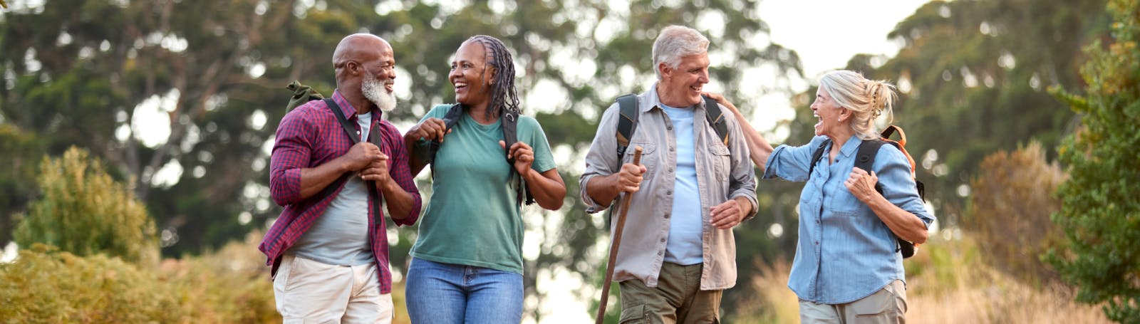 Over 60s couple travel break – smiling friends on a countryside walk with backpacks, perfect for senior holidays and insurance cover.