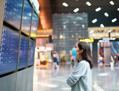 Frau mit Maske schaut auf eine Anzeige im Terminal