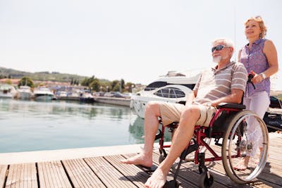 Reisen mit Behinderung: Frau schiebt einen Mann im Rollstuhl am Hafen.