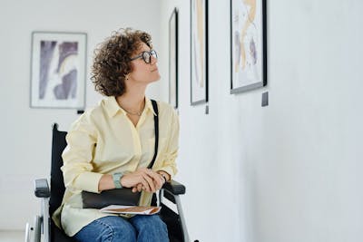 Ausflüge mit Rollstuhl: Frau im Rollstuhl schaut sich ein Bild in einer Ausstellung an.