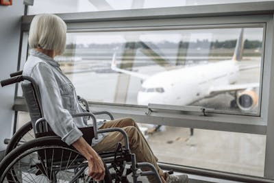 Frau im Rollstuhl blickt auf ein Flugzeug.